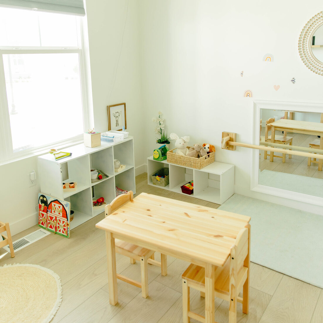 The small second room — white cubbies, a wooden table and chairs, a wall mirror with a ballet barre, and a soft mat.